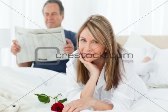 Happy woman with her rose while her husband is reading a newspaper