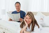 Smiling woman looking at the camera  while her husband is readin