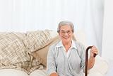 Mature woman sitting on the sofa with her walking stick