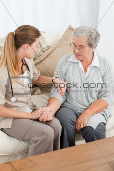 Beautiful nurse taking the pulse of her patient at home