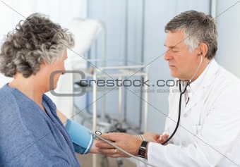 A senior doctor taking the blood pressure of his patient in his office