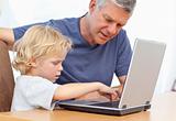 Lovely boy and his grandfather looking at their laptop at home