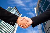 Business people shaking hands against blue sky and modern building