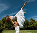 Young beautiful couple dance and embrace on grass over sky