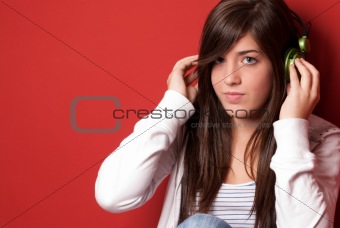 Young girl listening music with headphones on a red wall