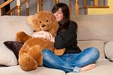 Young woman embracing teddy bear sitting on sofa