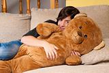 Young woman embracing teddy bear lying on on sofa