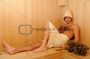 Young handsome man in a towel relaxing in a russian wooden sauna