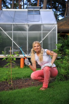 young pretty gardening woman with rakes outdoors near greenhouse