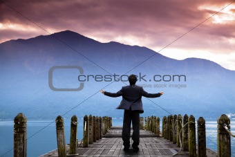Businessman stand on the pier  and watching the mountain and cloud of sunrise