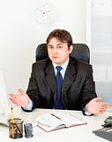 Confused modern businessman sitting at office desk
