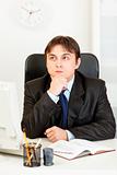 Thoughtful young businessman sitting at desk and planning timetable in diary
