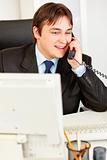 Successful modern businessman sitting at office desk and talking on phone
