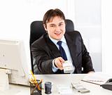 Smiling  businessman sitting at office desk and giving dollar pack

