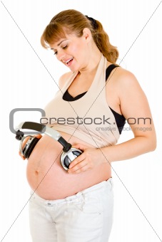 Happy pregnant woman holding headphones on her tummy
