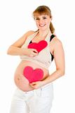 Happy pregnant woman holding two paper hearts in hands. Concept - two hearts beating in unison.  

