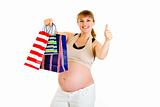 Happy pregnant woman holding shopping bags and showing thumbs up gesture

