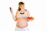Pensive pregnant woman making choice between pills and fruits
