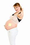Smiling pregnant woman with blank sticky note on her belly showing thumbs up gesture
