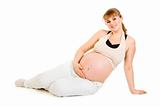 Happy beautiful pregnant woman sitting on floor and holding her belly 
