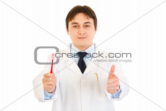 Smiling dentist holding toothbrush and showing  thumbs up gesture
