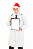 Smiling medical doctor in Santa hat holding blank clipboard
