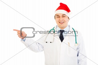 Medical doctor in hat of Santa Claus  pointing  finger in corner
