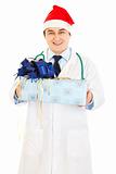 Smiling medical doctor in Santa hat holding present in hands 

