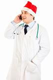 Smiling medical doctor in hat of Santa Claus talking on mobile phone
