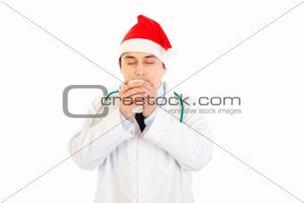 Medical doctor in Santa hat enjoying cup of hot coffee
