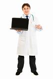 Smiling  doctor pointing finger on  laptop with blank screen
