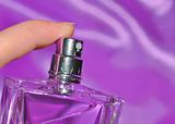 Woman hand spraying perfume over violet silk background