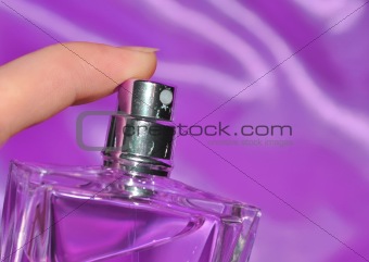 Woman hand spraying perfume over violet silk background