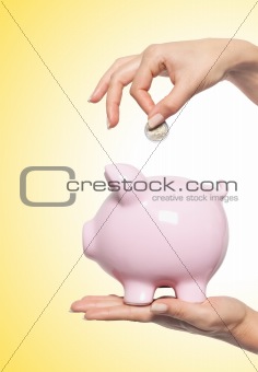 Hand putting money into the piggy bank over yellow background