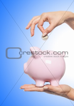 Hand putting money into the piggy bank over blue