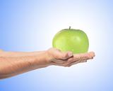 Green apple on man's hand over blue background