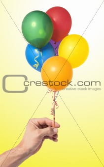 Hand holding colorful air balloons over yellow background