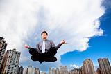 Businessman meditating in the air before modern building