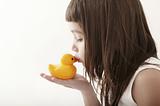 little toddler girl kissing a yellow bath duck