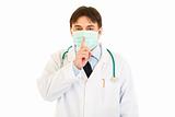 Medical doctor with  mask on face holding finger at mouth. Shh gesture
