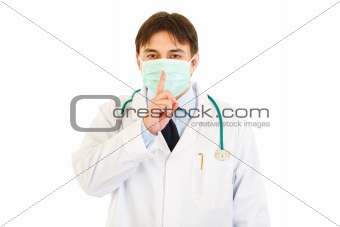 Medical doctor with  mask on face holding finger at mouth. Shh gesture
