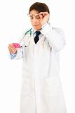 Concentrated doctor raising eyeglasses and reading name of drug
