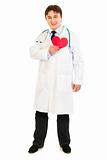 Smiling medical doctor holding paper heart near  chest
