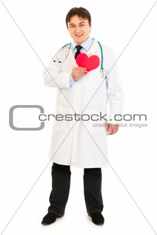 Smiling medical doctor holding paper heart near  chest
