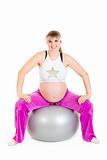 Smiling beautiful pregnant female doing exercises on fitness ball

