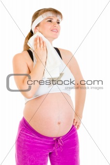 Smiling pregnant female wiping her face with towel after exercising

