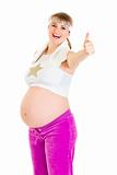 Smiling beautiful pregnant female in sportswear showing thumbs up gesture
