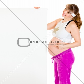 Smiling beautiful pregnant woman pointing finger at blank billboard
