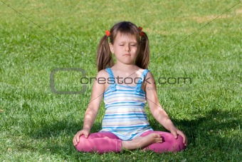 Little child sit and meditate in asana on green grass