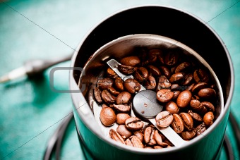 Electrical coffee-mill machine with roasted coffee beans on the green tabletop with top cover removed
